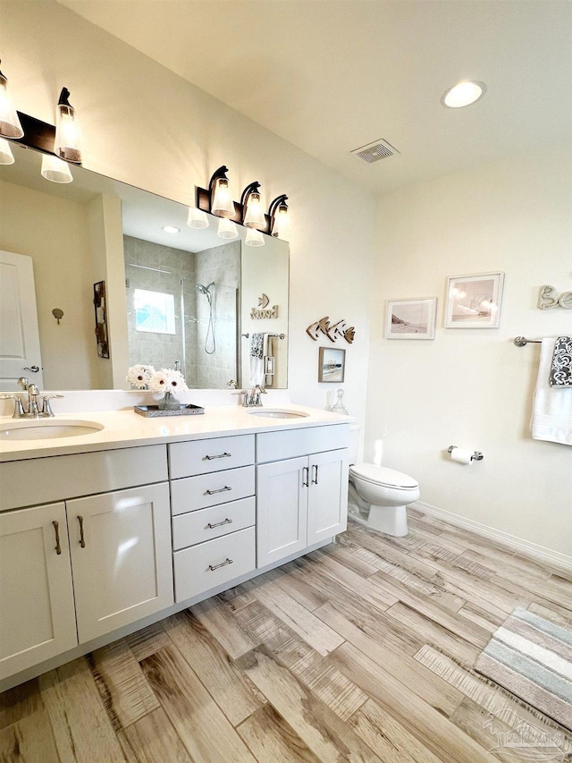 bathroom with tiled shower, vanity, toilet, and wood-type flooring