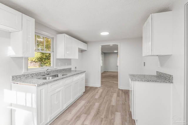 kitchen with light wood-type flooring, a textured ceiling, white cabinetry, and sink