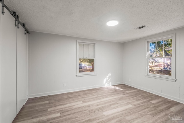 spare room with a barn door, light hardwood / wood-style flooring, and a textured ceiling