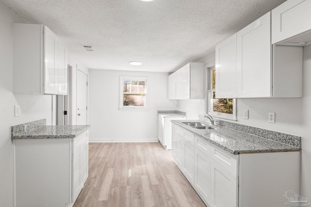 kitchen featuring light stone counters, sink, white cabinets, and a healthy amount of sunlight