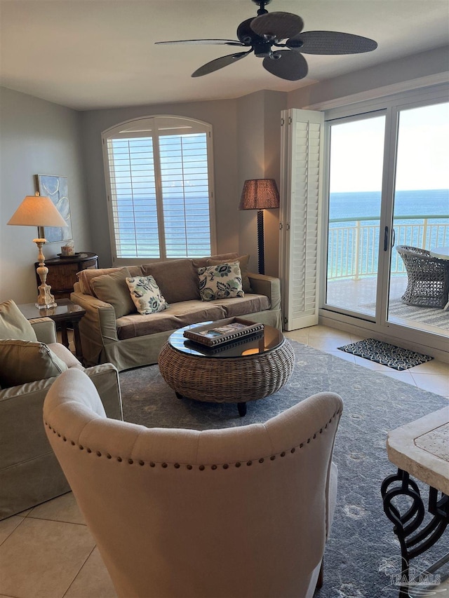 tiled living room with ceiling fan and a water view