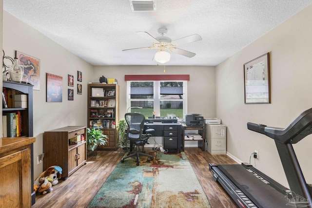 home office with a textured ceiling, wood finished floors, visible vents, and a ceiling fan