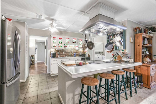 kitchen with visible vents, white cabinets, decorative backsplash, a breakfast bar, and freestanding refrigerator