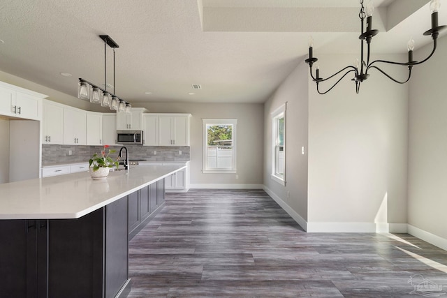 kitchen featuring tasteful backsplash, light countertops, stainless steel microwave, a notable chandelier, and white cabinetry