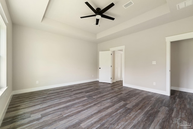 unfurnished room with visible vents, dark wood-type flooring, a tray ceiling, and ceiling fan