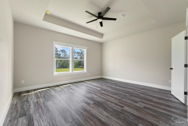 spare room with baseboards, a ceiling fan, a tray ceiling, and dark wood finished floors