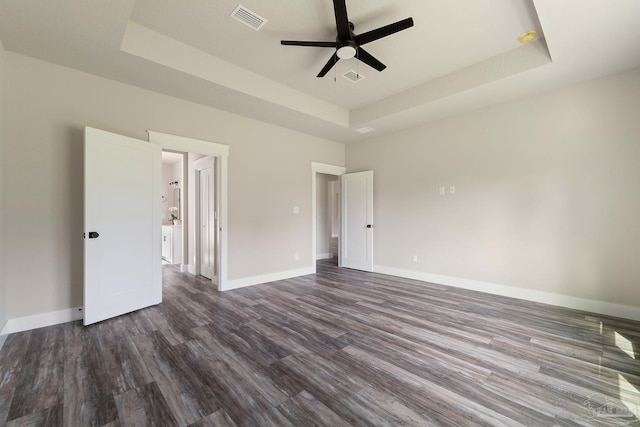 unfurnished room with ceiling fan, visible vents, baseboards, a tray ceiling, and dark wood-type flooring