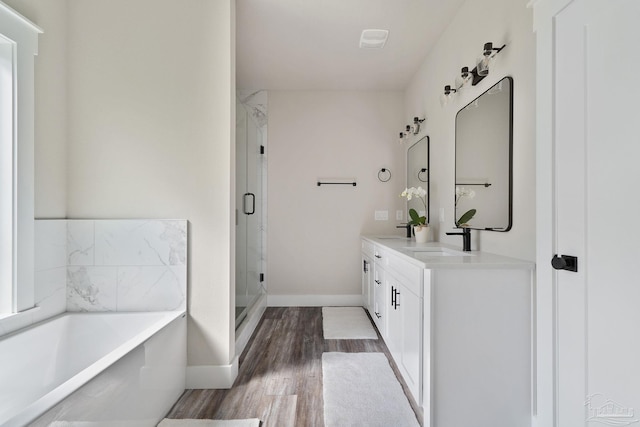 full bath featuring a sink, double vanity, baseboards, wood finished floors, and a garden tub