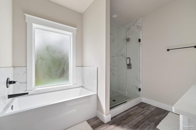 full bath with baseboards, a marble finish shower, a garden tub, and wood finished floors