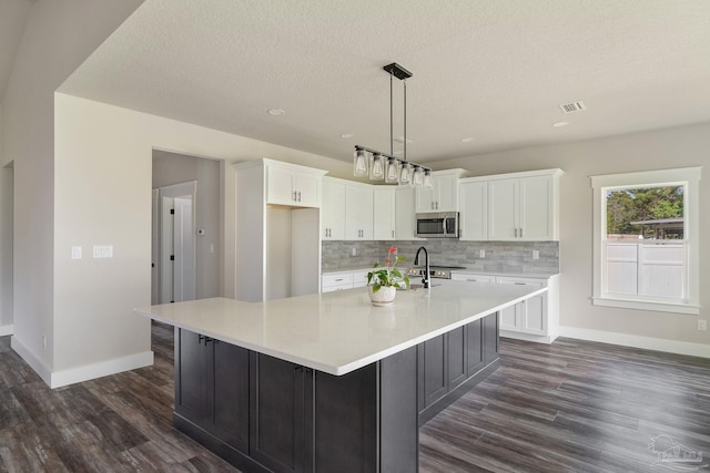 kitchen with a large island with sink, baseboards, stainless steel appliances, white cabinetry, and dark wood-type flooring