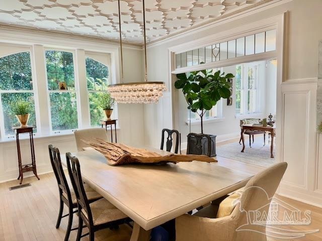 dining room with ornamental molding, light hardwood / wood-style flooring, a notable chandelier, and a healthy amount of sunlight