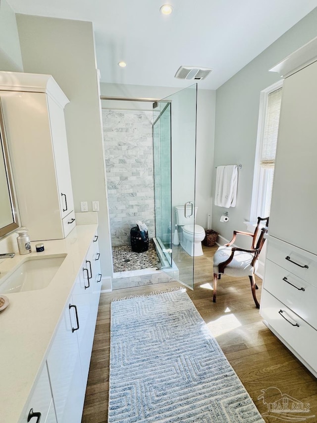 bathroom with vanity, hardwood / wood-style floors, a shower with shower door, and toilet