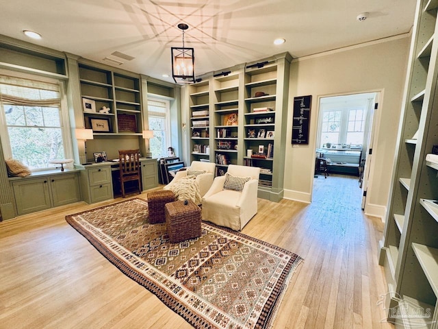 living area with an inviting chandelier, light hardwood / wood-style flooring, a healthy amount of sunlight, and built in desk