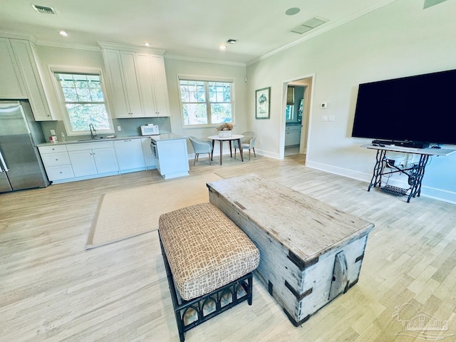 kitchen with white cabinetry, stainless steel refrigerator, ornamental molding, light hardwood / wood-style floors, and sink