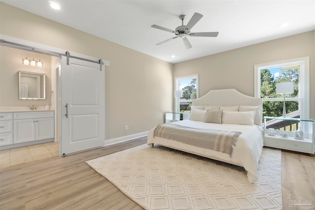 bedroom featuring a barn door, ceiling fan, light wood-type flooring, and connected bathroom