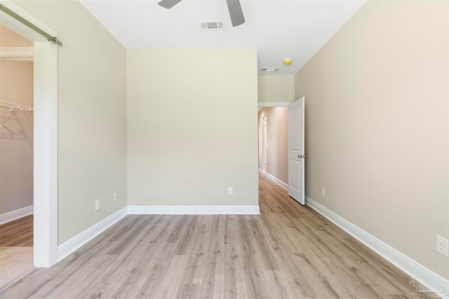 unfurnished bedroom featuring ceiling fan, a walk in closet, a closet, and light hardwood / wood-style floors