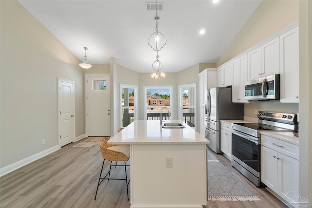 kitchen featuring white cabinetry, decorative light fixtures, sink, appliances with stainless steel finishes, and a center island with sink