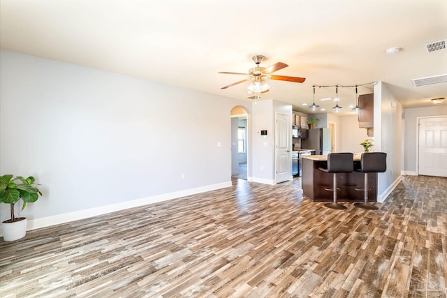 living area featuring visible vents, a ceiling fan, wood finished floors, arched walkways, and baseboards
