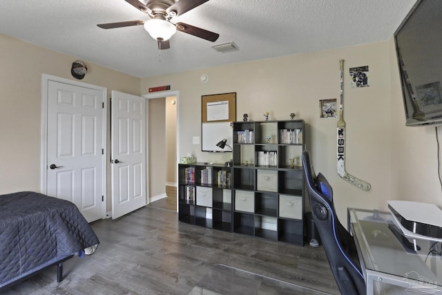 bedroom with ceiling fan, a textured ceiling, visible vents, and wood finished floors