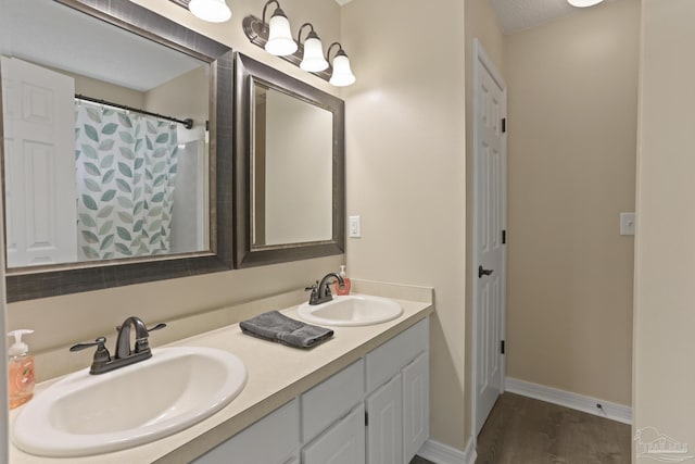 full bath with baseboards, double vanity, a sink, and wood finished floors