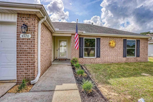 property entrance featuring a lawn, a shingled roof, brick siding, and a garage