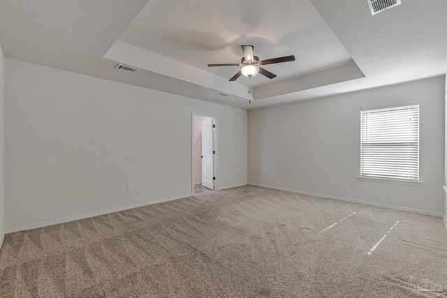 empty room with a tray ceiling, ceiling fan, and light colored carpet