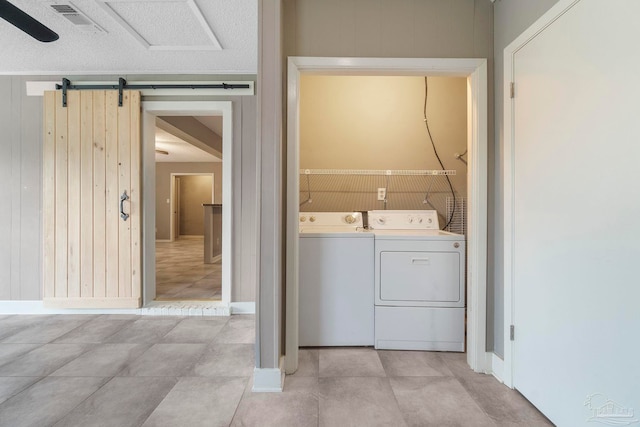 laundry area featuring washer and dryer, a barn door, light tile patterned floors, and a textured ceiling