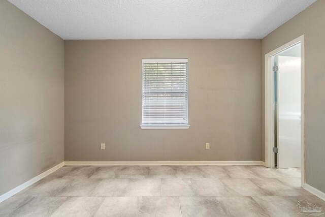 tiled empty room featuring a textured ceiling