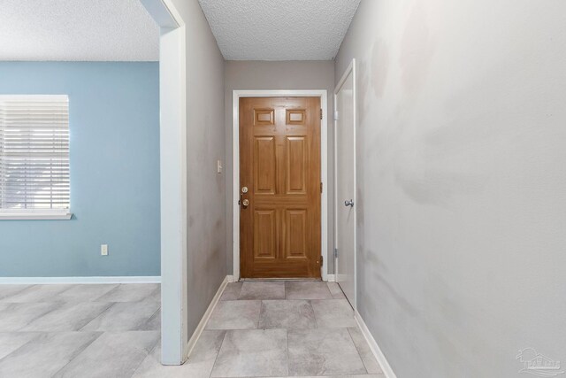 hallway with a textured ceiling and light tile patterned floors