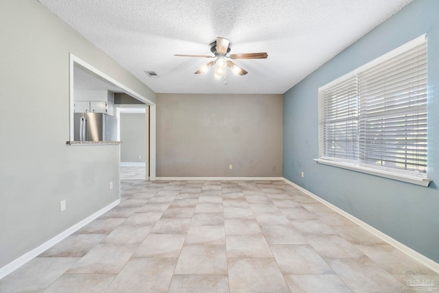 spare room featuring a textured ceiling, ceiling fan, and light tile patterned floors