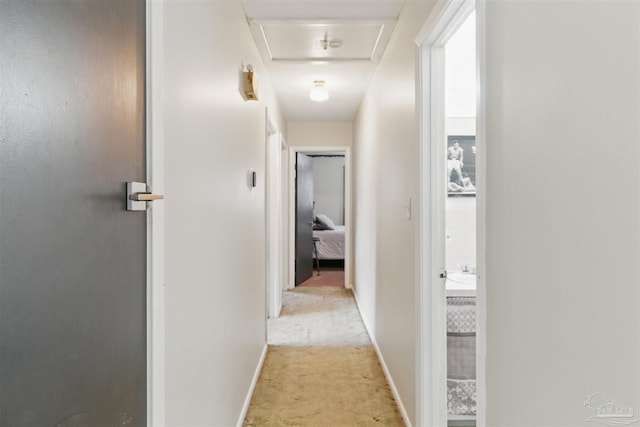 hall with attic access, baseboards, and light carpet
