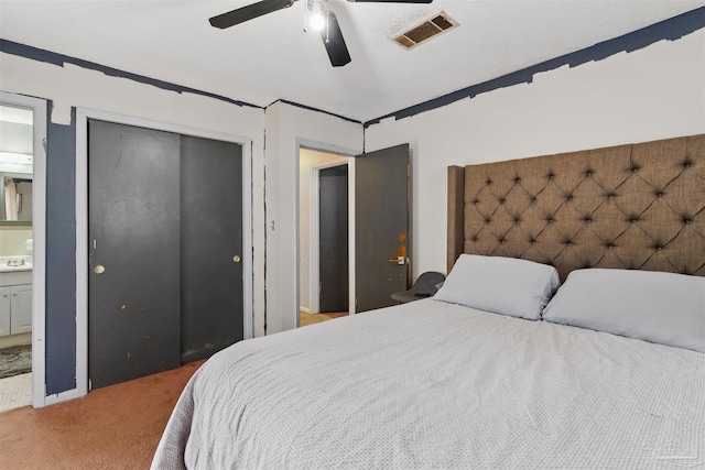 carpeted bedroom with ensuite bathroom, visible vents, a closet, and ceiling fan