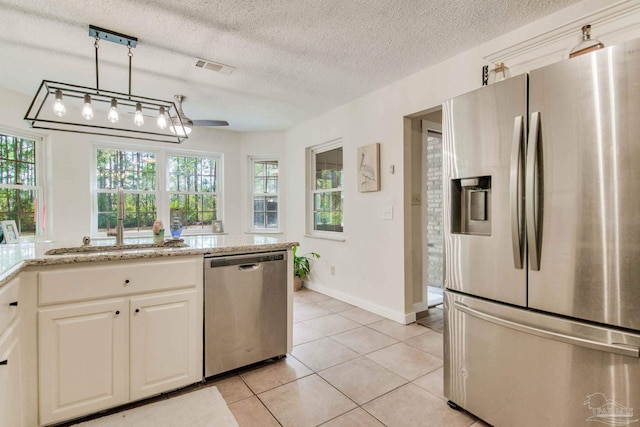 kitchen with decorative light fixtures, light stone counters, a textured ceiling, and appliances with stainless steel finishes