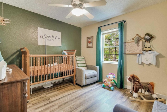 bedroom with a crib, wood-type flooring, a textured ceiling, and ceiling fan