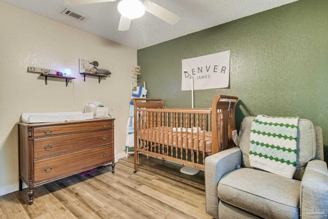 bedroom featuring a textured ceiling, ceiling fan, light hardwood / wood-style flooring, and a nursery area