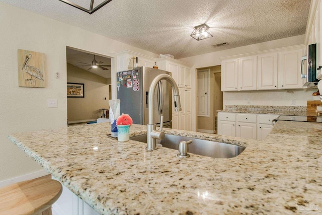 kitchen featuring a breakfast bar, ceiling fan, stainless steel fridge, light stone countertops, and a textured ceiling