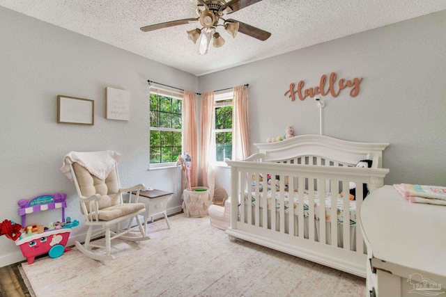 bedroom with a crib, a textured ceiling, and ceiling fan