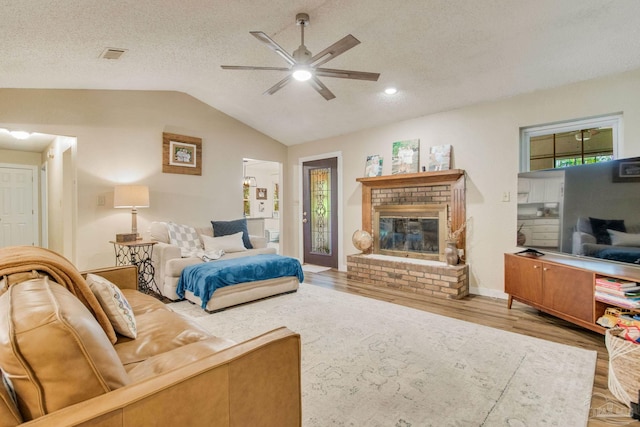 bedroom featuring ceiling fan, light hardwood / wood-style floors, lofted ceiling, a textured ceiling, and a fireplace