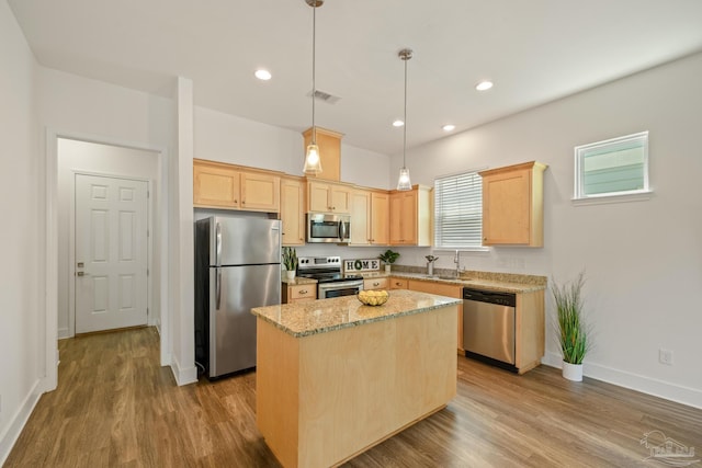 kitchen with stainless steel appliances, a sink, light brown cabinetry, a kitchen island, and wood finished floors