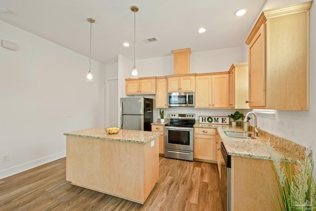 kitchen with appliances with stainless steel finishes, a sink, light brown cabinetry, light wood-style flooring, and a center island