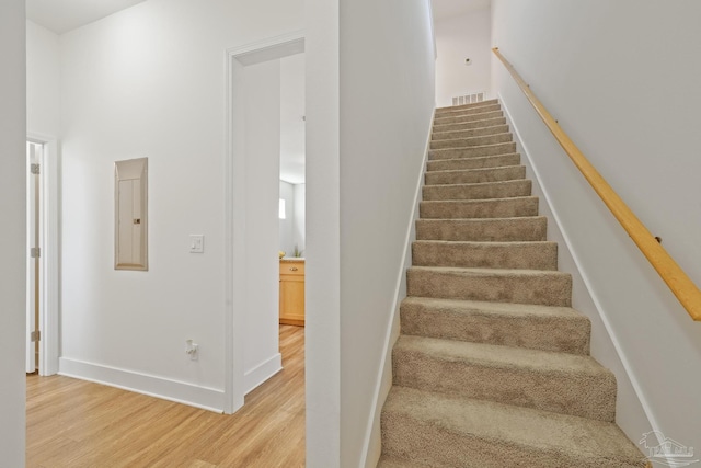 stairway featuring wood finished floors, electric panel, and baseboards