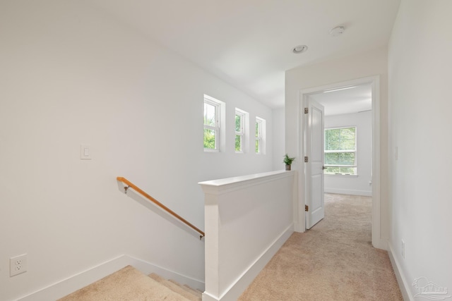 hall with an upstairs landing, light carpet, and baseboards