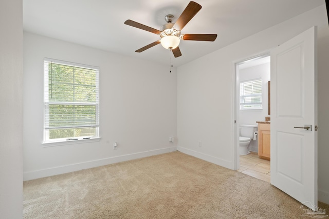 unfurnished bedroom featuring light colored carpet, baseboards, ensuite bathroom, and a ceiling fan