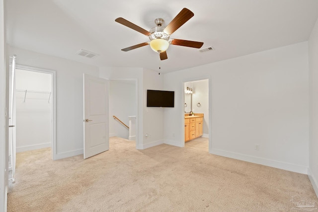 unfurnished bedroom featuring light carpet, baseboards, a walk in closet, a closet, and ceiling fan