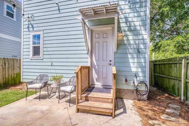 view of exterior entry with fence and a patio area