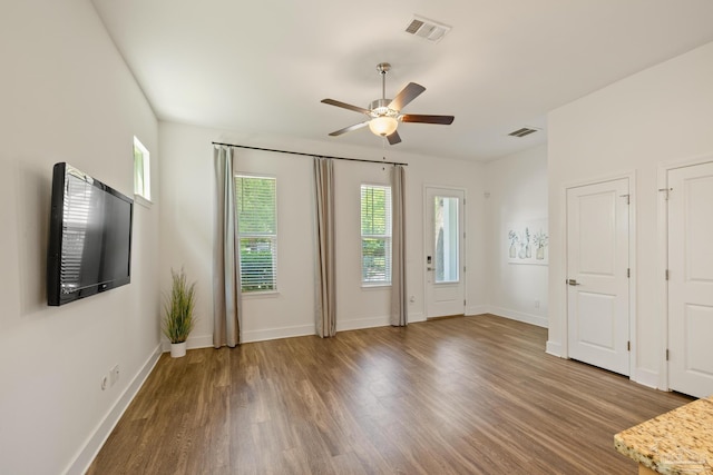 unfurnished living room with a ceiling fan, plenty of natural light, wood finished floors, and baseboards