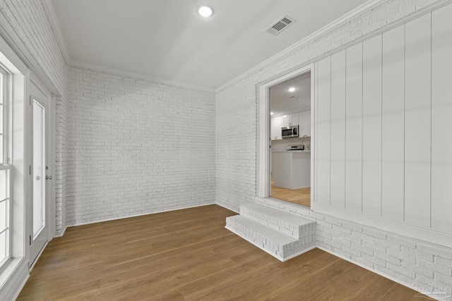 spare room with visible vents, wood finished floors, brick wall, and crown molding