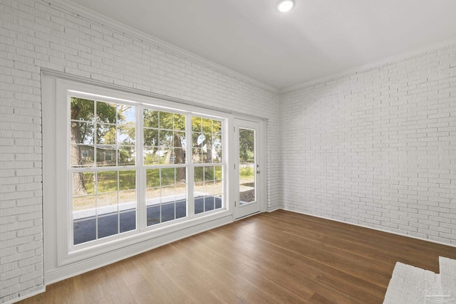 empty room featuring wood finished floors, brick wall, and crown molding