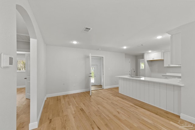 kitchen featuring visible vents, a sink, white cabinetry, arched walkways, and light countertops