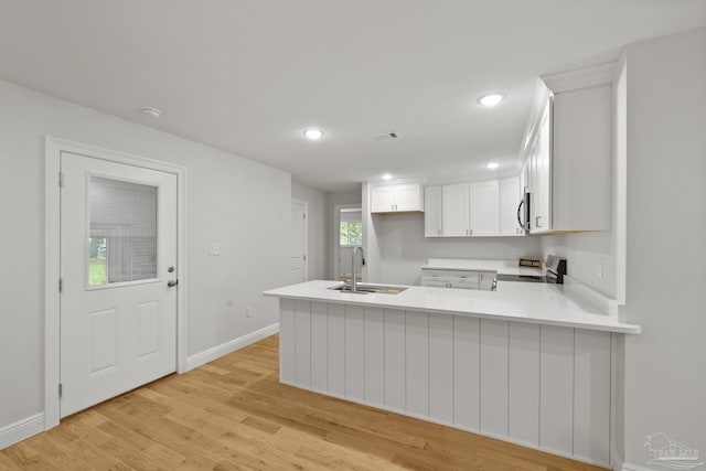 kitchen with light countertops, light wood-style flooring, appliances with stainless steel finishes, a peninsula, and a sink